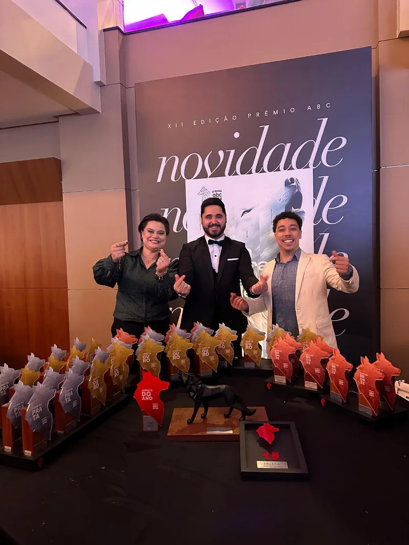 Alex Pinhol e dois sócios da Agência WB.P atrás da mesa com os troféus Lobo de
            Ouro, de Prata e de Bronze da XII edição do Prêmio ABC, com a placa Agência do Ano
            de 2024 à frente