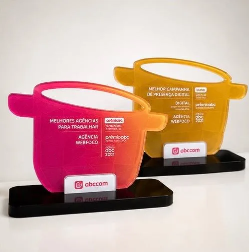Os dois troféus do Prêmio ABC 2021 lado a lado: o rosa de Melhores Agências
              Para Trabalhar e o dourado de Melhor Campanha de Presença Digital, ambos gravados
              com o nome Agência Webfoco